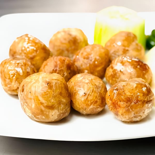 A close-up of several golden-brown Thai meatballs on a white plate with a cucumber slice.