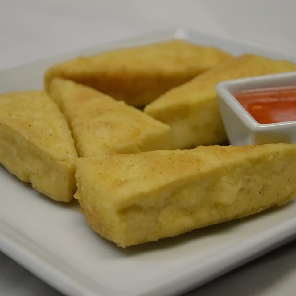 Golden fried tofu triangles with a side of sweet chili dipping sauce on a white plate.