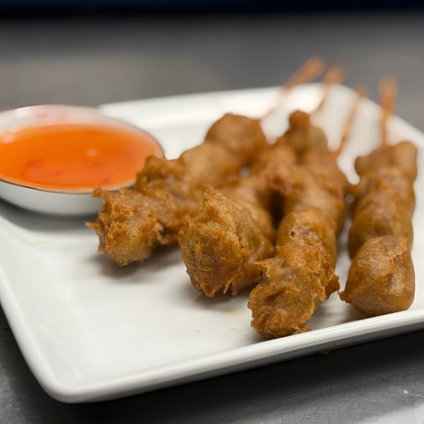 Omaha Mercy Thai's fried chicken skewers with sweet chili dipping sauce on a white plate.