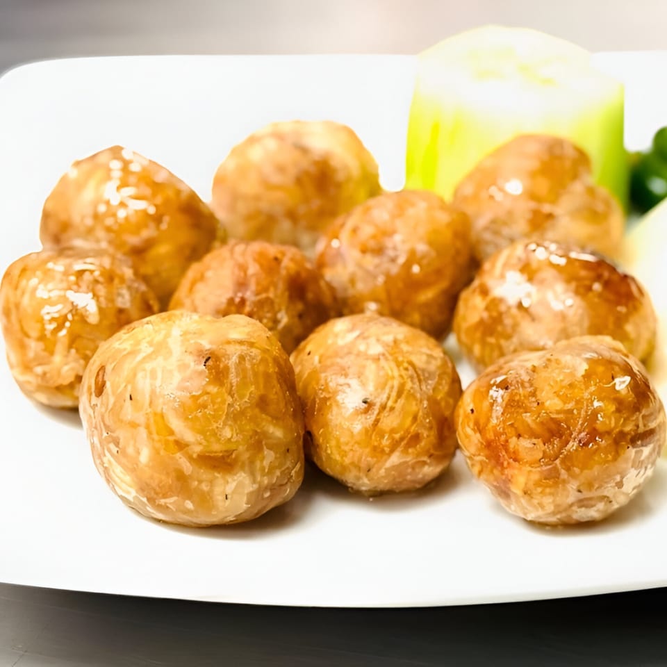 A plate of golden-brown Thai meatballs, garnished with a slice of cucumber and a sprig of parsley.