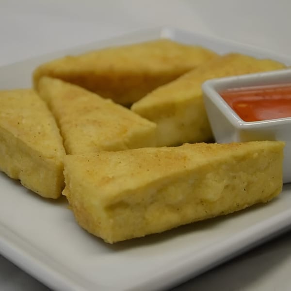 Golden fried tofu triangles with a side of sweet chili dipping sauce on a white plate.