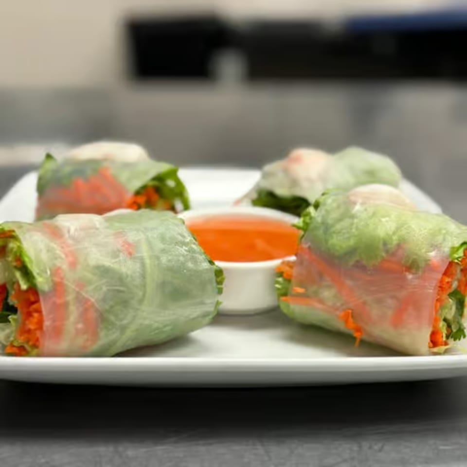 Fresh Thai spring rolls with lettuce, carrots, and a sweet chili dipping sauce on a white plate.