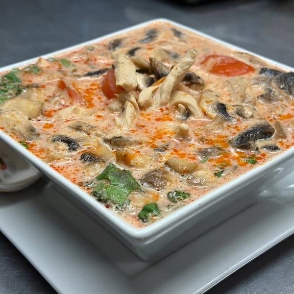 Close-up of a square bowl of Tom Kha Gai soup with chicken, mushrooms, and tomatoes.