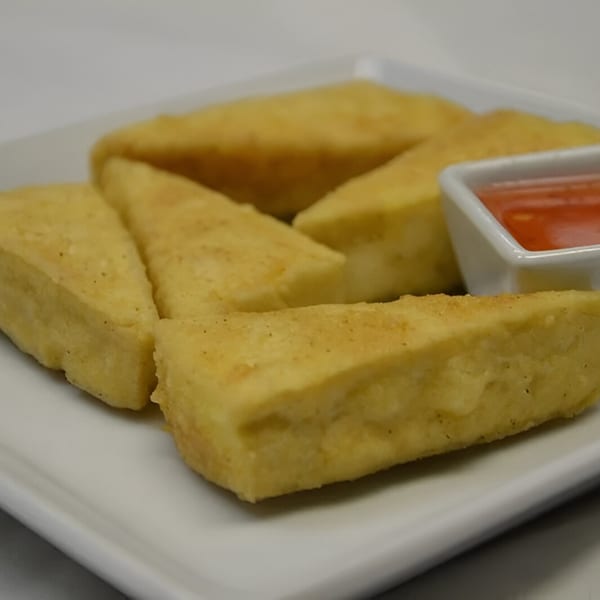 Golden fried tofu triangles with a side of sweet chili dipping sauce on a white plate.